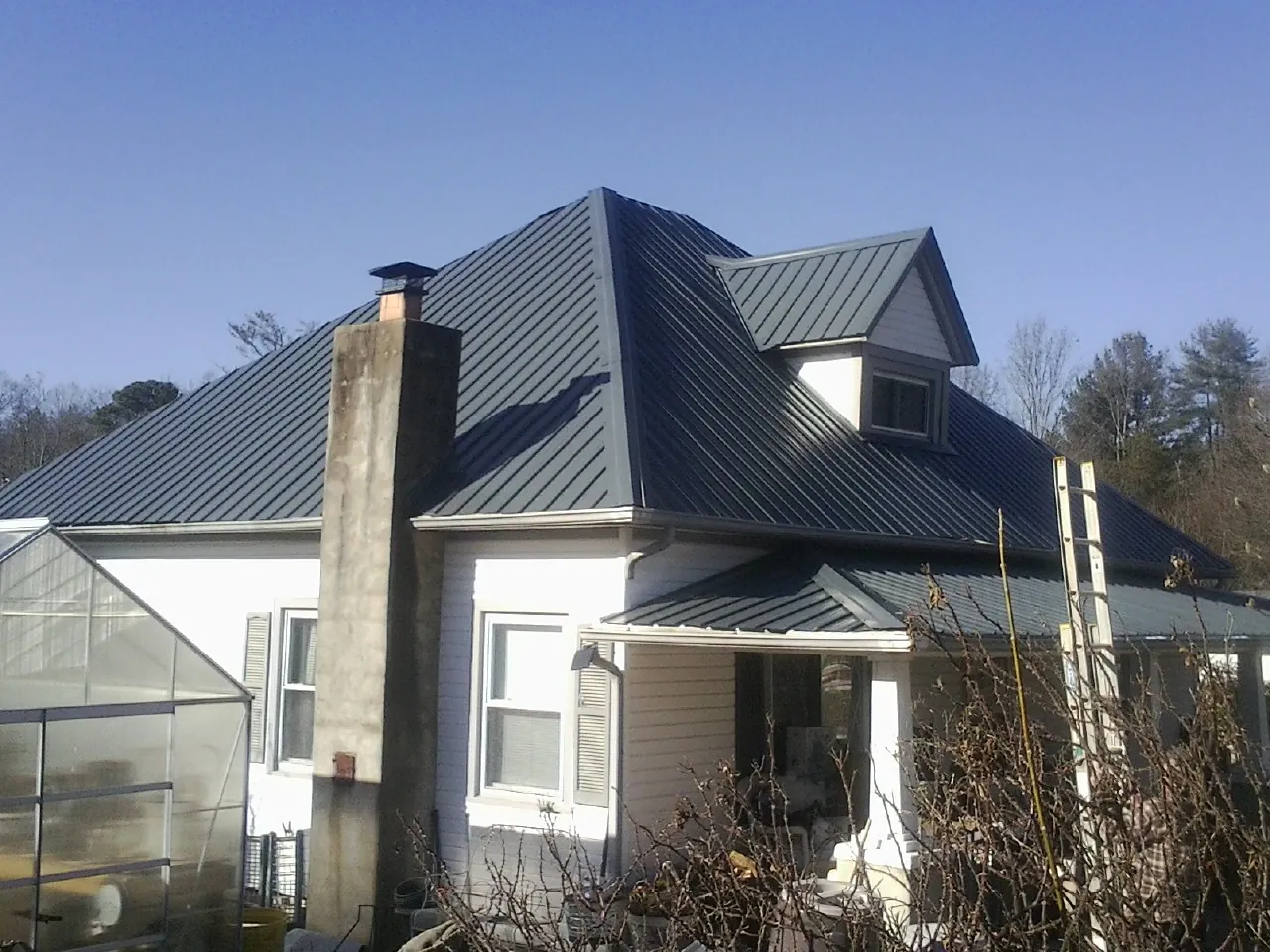 Dark blue standing seam metal roof on a white farmhouse with dormer — Slate & Tile Roof Repair by Roofing Brothers in Penrose