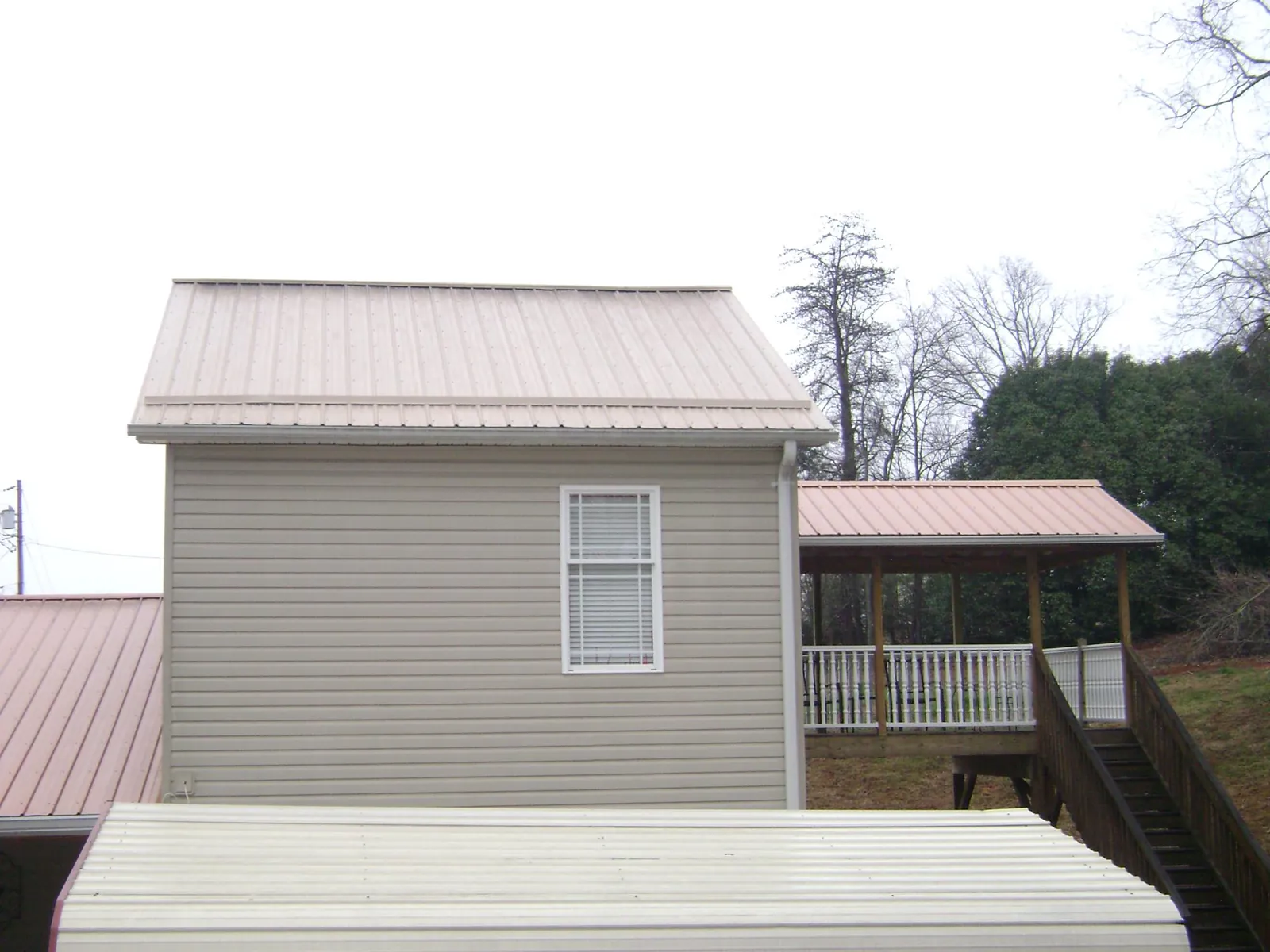 Tan metal roofs on a two story addition and attached porch, from a Roof Replacement job in Penrose